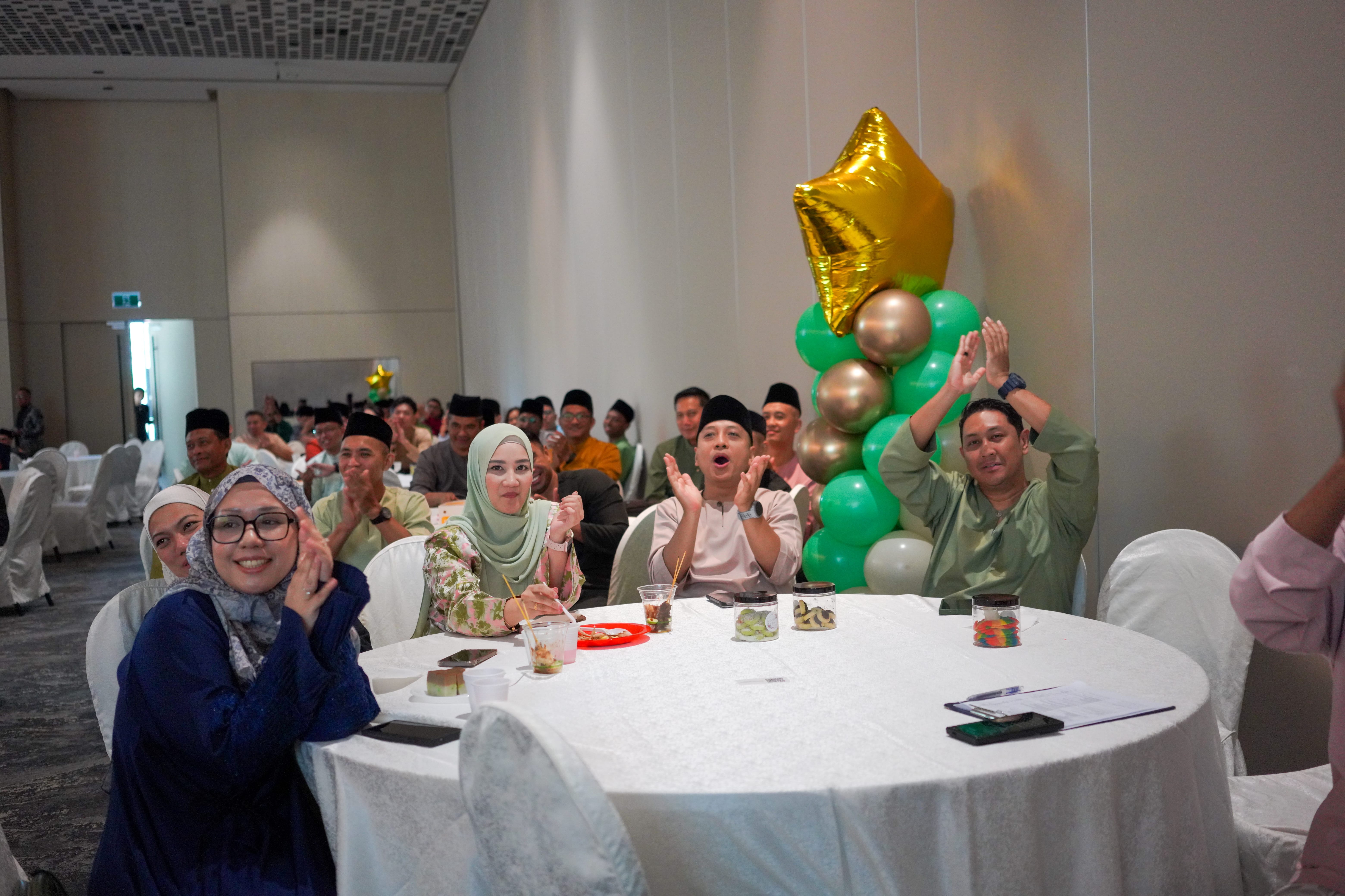Attendees seated at a banquet table applauding and cheering during a stage performance.
